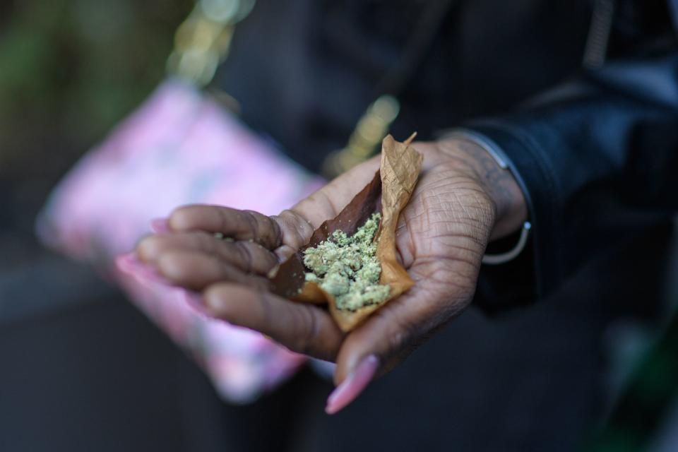 A woman holds out her hand with the makings for a smoke, with tobacco leaf and buds.