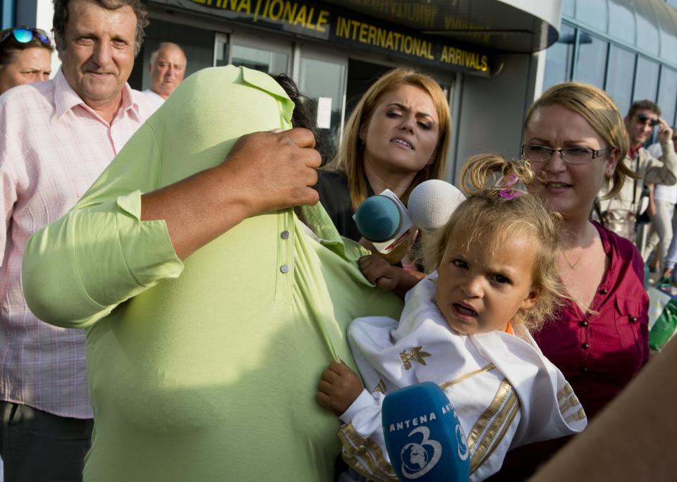 Surrounded by media, a Romanian Roma woman expelled from France covers her head while holding a baby upon arriving at Bucharest's Henri Coanda international airport in Otopeni, Romania, Thursday, Sept. 13, 2012. French Interior Minister Manual Valls, on a two-day official visit to Romania, is in discussions with Romanian authorities on the issue of Roma immigration to France and ways to support Roma inclusion. (AP Photo/Vadim Ghirda)
