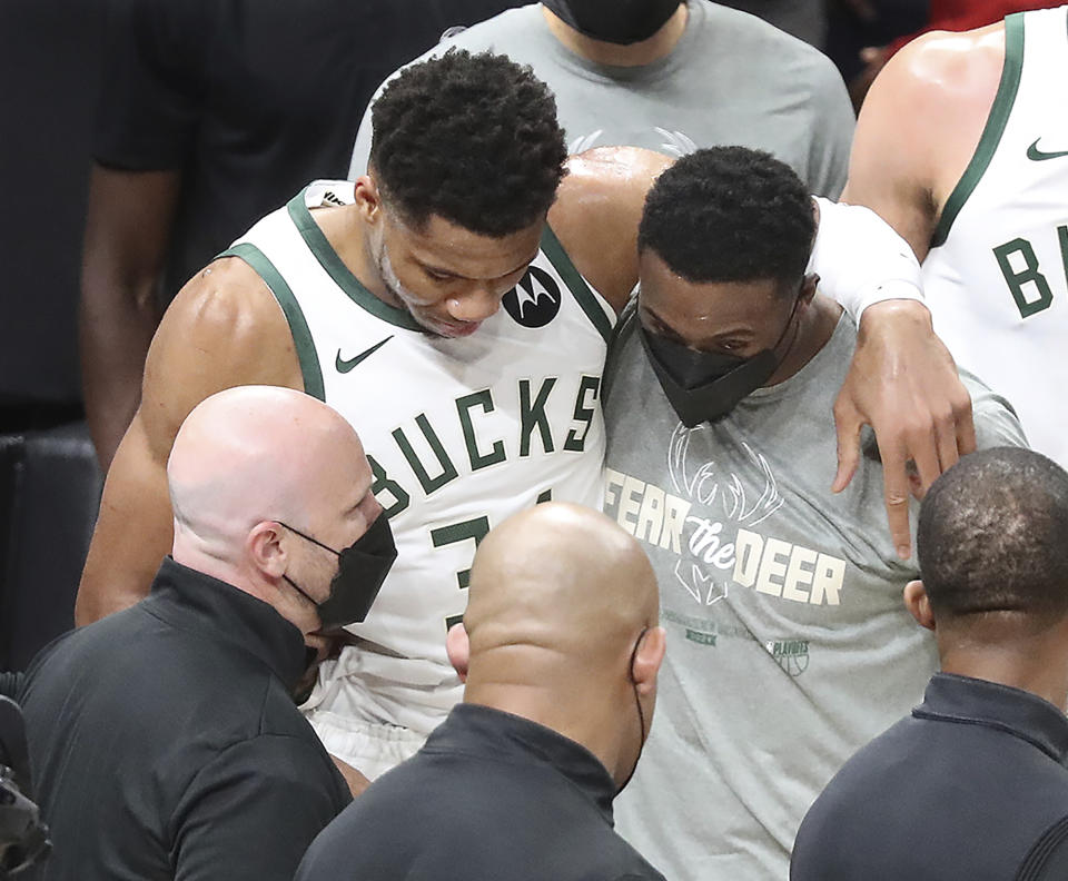 Milwaukee Bucks forward Giannis Antetokounmpo is helped up by his brother Thanasis Antetokounmpo (right), who also plays for the team, after he hyperextended his left knee on this play hitting the floor after rising to challenge a slam by Atlanta Hawks center Clint Capela on a lob pass by Lou Williams with 7:14 left in the third quarter of game 4 in the NBA Eastern Conference Finals on Tuesday, June 29, 2021, in Atlanta. (Curtis Compton/Atlanta Journal-Constitution via AP)