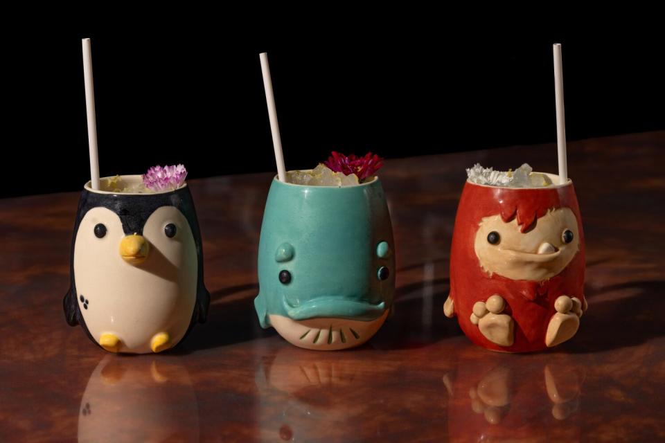 Three ceramic cups in the shapes of a penguin, a whale and a monkey, with straws