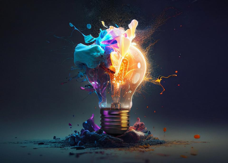 An artistic picture of a light bulb exploding into blue and purple paint against a black backdrop.