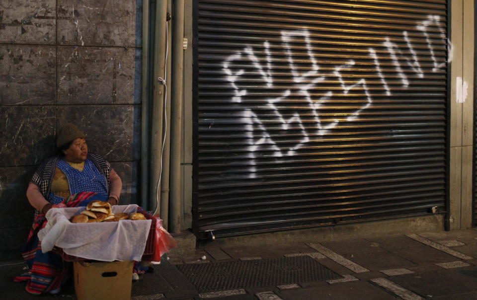 Una mujer vende pan en una calle al lado de un negocio con una pintada contra el presidente Evo Morales en La Paz, Bolivia, el miércoles 6 de noviembre de 2019. (AP Foto / Juan Karita)