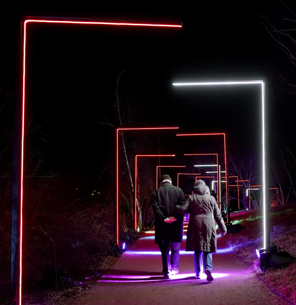 An elderly couple walks through the "Half Arches" light display created by Culture Creative, part of the Chicago Botanic Garden's 1.3-mile Lightscapes holiday experience of light and music in Glencoe, Ill., on Thursday, Dec. 14, 2023. (AP Photo/Charles Rex Arbogast)