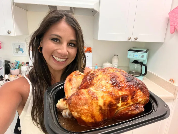 The writer holds the Costco rotisserie chicken. Liquid can be seen at the bottom of the plastic container the chicken sits in