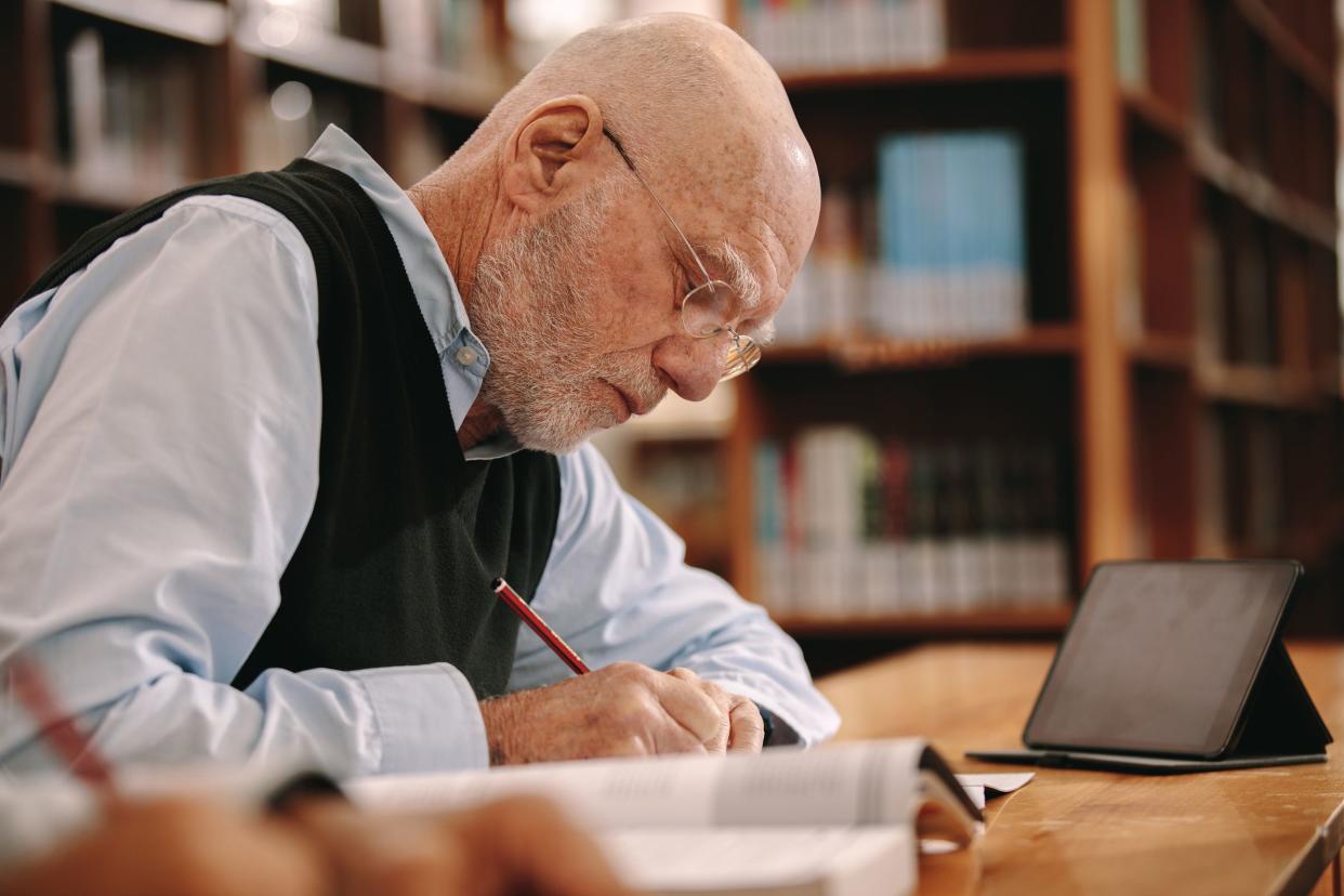 senior man writing notes sitting in library