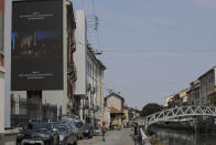 Pedestrians pass by a screen advertising the Milan Digital Fashion Week, in Milan, Italy, Tuesday, July 14, 2020. Forty fashion houses are presenting previews of menswear looks for next spring and summer and pre-collections for women in digital formats, due to concerns generated by the COVID-19. (AP Photo/Luca Bruno)