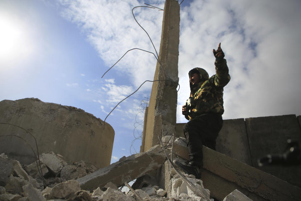 A Kurdish-led Syrian Democratic Forces fighter, stands at a damgaed part of the defense wall of Gweiran Prison, in Hassakeh, northeast Syria, Sunday, Jan. 23, 2022. Clashes between U.S.-backed Syrian Kurdish fighters and militants continued for a fourth day Sunday near a prison in northeastern Syria that houses thousands of members of the Islamic State group, the Kurdish force said. (AP Photo/Hogir Al Abdo)