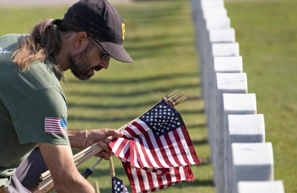 Volunteer Joe Schwann places American flags in front of headstones at the South Florida National Cemetery in Lake Worth on Sunday to honor U.S. military veterans.