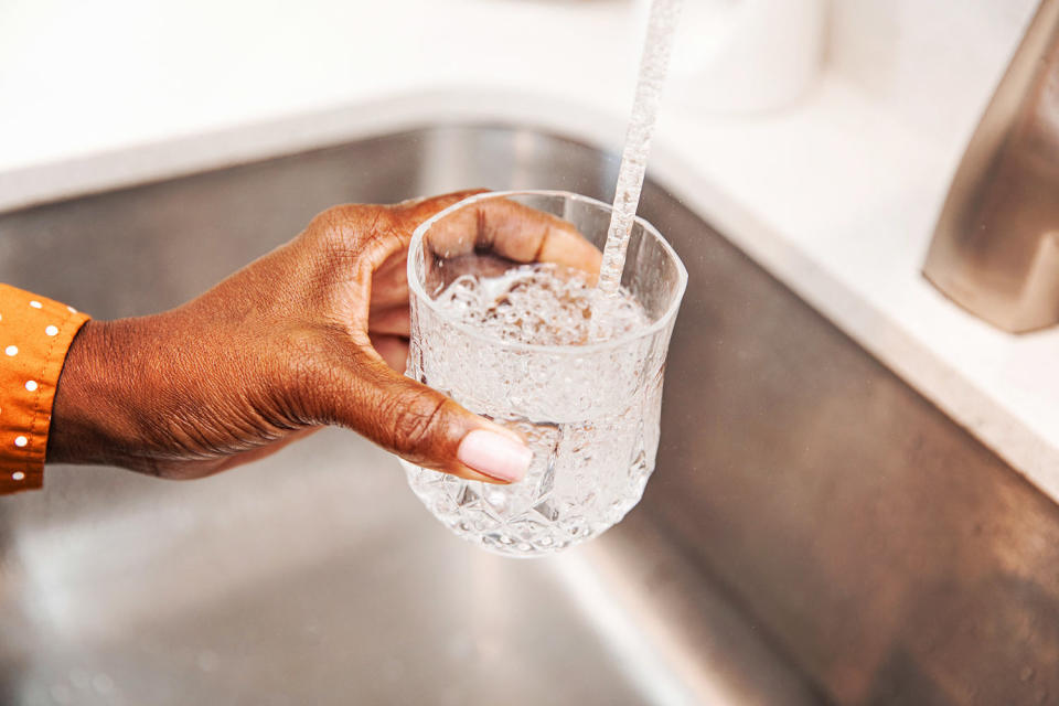 Woman pouring herself a glass of tap water from the kitchen sink (vitapix / Getty Images)