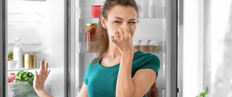 Young woman feeling bad smell from refrigerator in kitchen