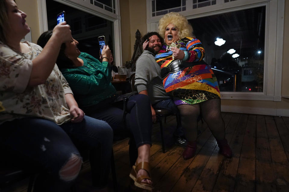 La drag queen Alexus Daniels interpreta "Heart of Glass" de Blondie sentada en regazo de un integrante de la audiencia que sonrie y dio su consentimiento mientras otros toman fotografías durante el espectáculo "Daniels Family Values" en el Heritage Restaurant en Shamokin, Pensilvannia, el 16 de abril de 2022. Daniels, la matriarca de una familia dra, es hija de un miero de carbó y una trabajadora textil que nació con "un espíritu femenino". Trabaja en un hospital local. (Foto AP/Carolyn Kaster)