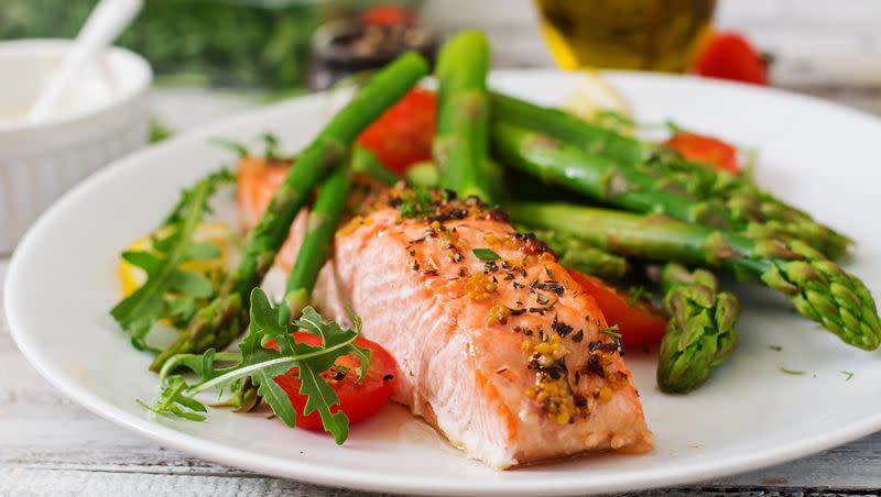 Baked salmon garnished with asparagus and tomatoes with herbs. Fish and vegetables are among foods that promote brain health.
