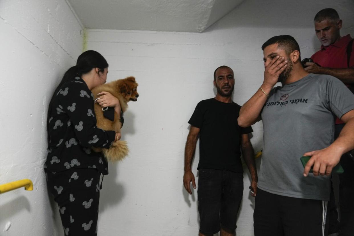A woman, holding a small dog, and a few men stand in a room with white walls