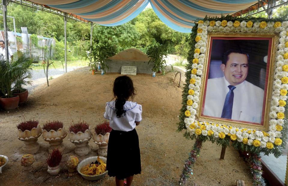 In this Nov. 20, 2016 photo, a girl stands by a portrait of Kem Ley, a Cambodian prominent political analyst, at his grave in Ang Takok, Cambodia. Kem Ley, a poor rice farmer's son turned champion of Cambodia's have-nots, was sipping his usual iced latte in the same chair he had occupied most mornings for years when a former solider he may never have met walked into the Caltex gas station cafe. Armed with a semi-automatic Glock pistol, the assassin fired into his chest and head, execution-style. Then he walked casually away from the scene. (AP Photo/Denis Gray)