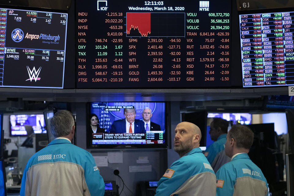 FILE - In this March 18, 2020, file photo traders at the New York Stock Exchange watch President Donald Trump's televised White House news conference in New York. When President Donald Trump speaks, financial markets gyrate and quiver in real time. (AP Photo/Mark Lennihan, File)