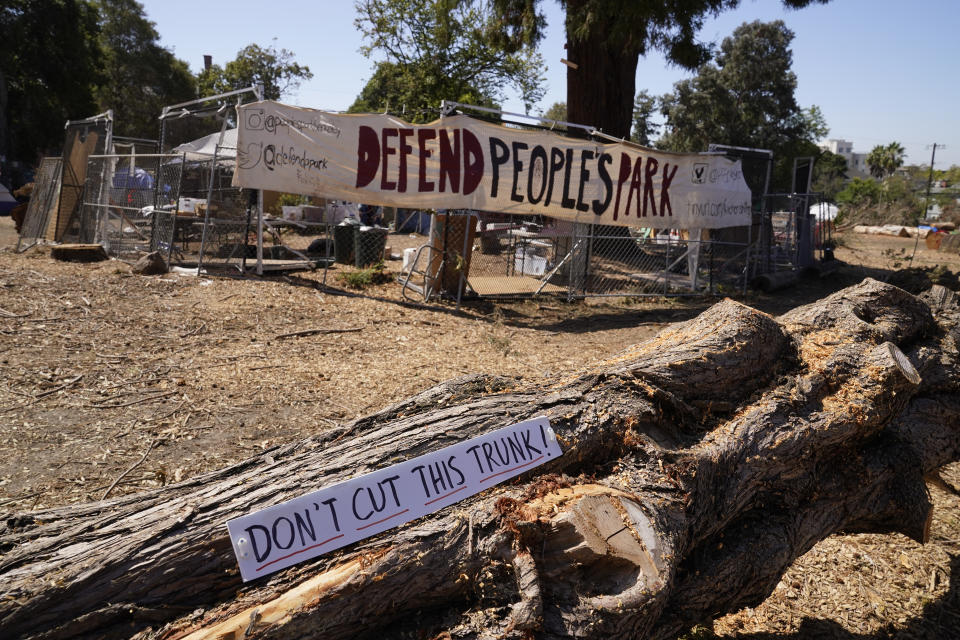 A fallen tree sits by a newly-erected barricade at People's Park in Berkeley, Calif., Tuesday, Aug. 16, 2022. The three-acre site's colorful history, forged from University of California, Berkeley's seizure of the land in 1968, has been thrust back into the spotlight by the school's renewed effort to pave over People's Park as part of a $312 million project that includes sorely needed housing for about 1,000 students. (AP Photo/Eric Risberg)
