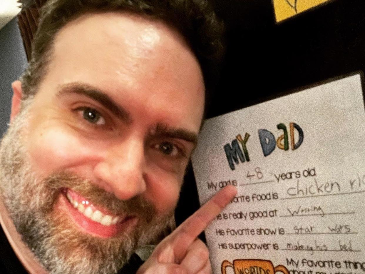 Man pointing to his daughter's school project about her dad on the wall.