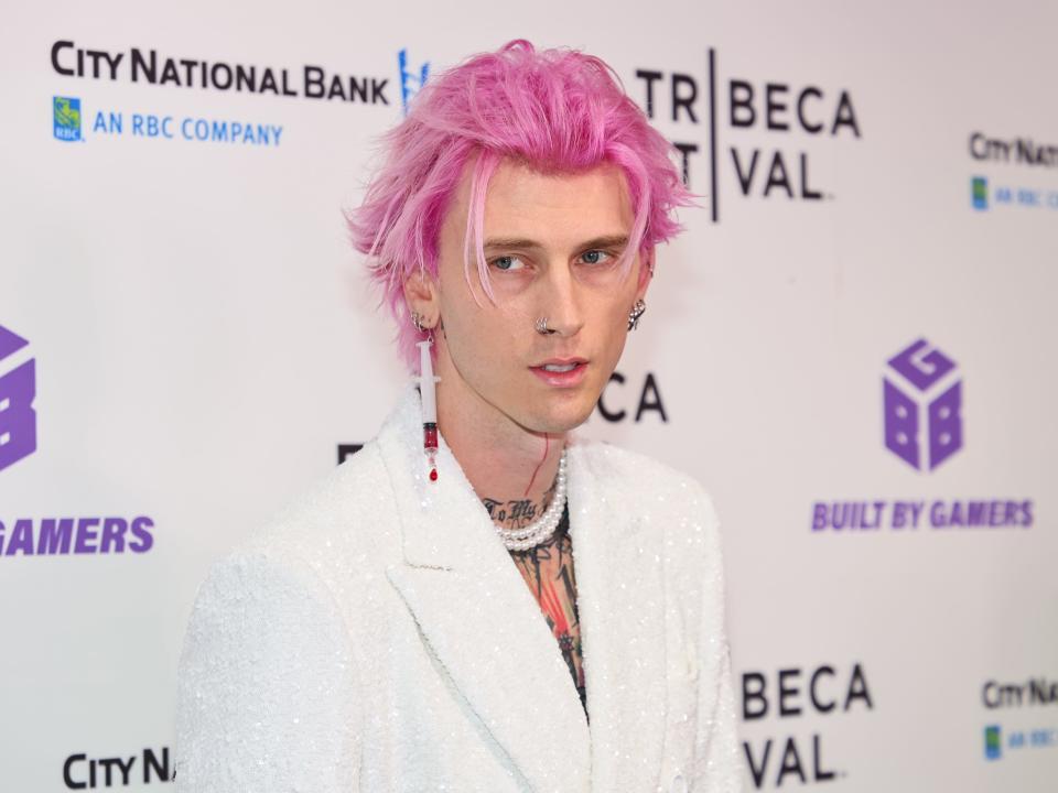 machine gun kelly on the red carpet for taurus, with a syringe earring dangling from his ear, filled with some kind of red liquid