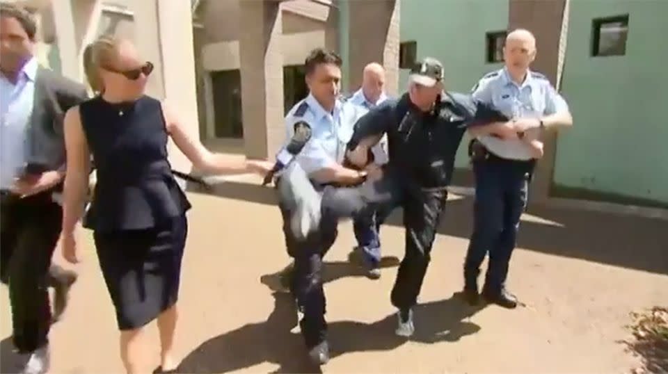 The 78-year-old was escorted away after he attempted to hurl a walking stick at the media. Source: 7 News