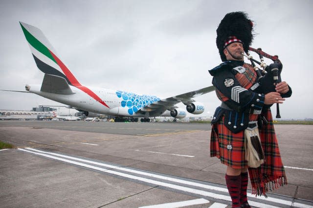 An Emirates A380 and a man playing bagpipes at Glasgow Airport