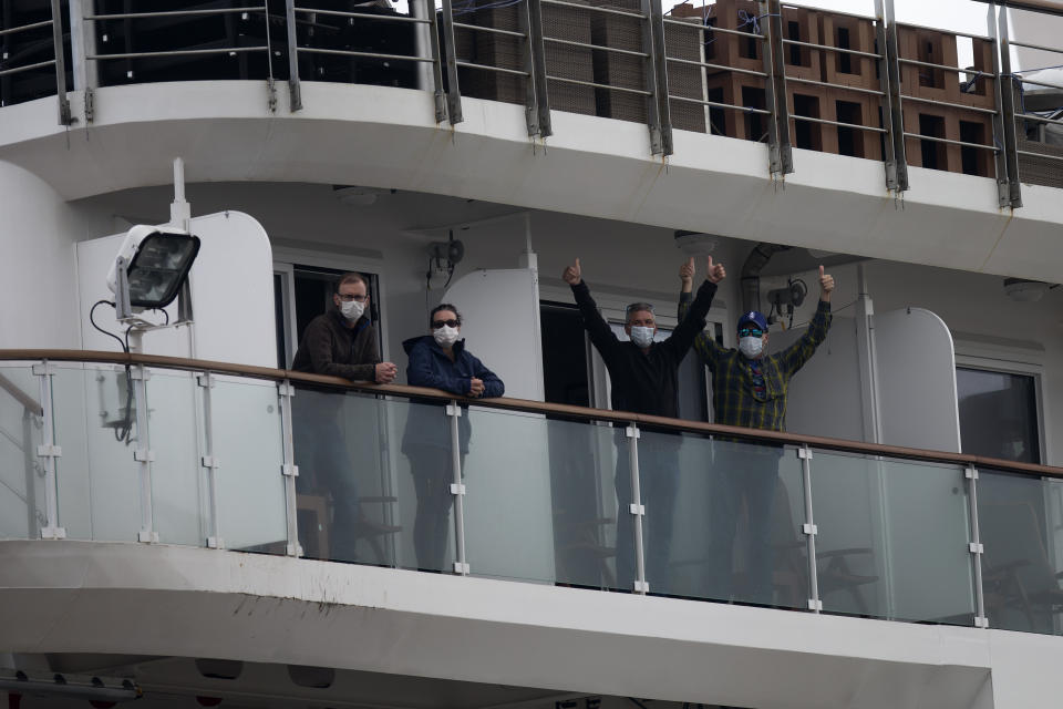 Passengers on the Australian cruise ship "Greg Mortimer" give thumbs up from a balcony as they arrive to disembark and make their way to the international airport in Montevideo, Uruguay, Wednesday, April 15, 2020. The ship has been anchored off Uruguay's coast since March 27 with more than half its passengers and crew infected with the new coronavirus, according to authorities. (AP Photo/Matilde Campodonico)