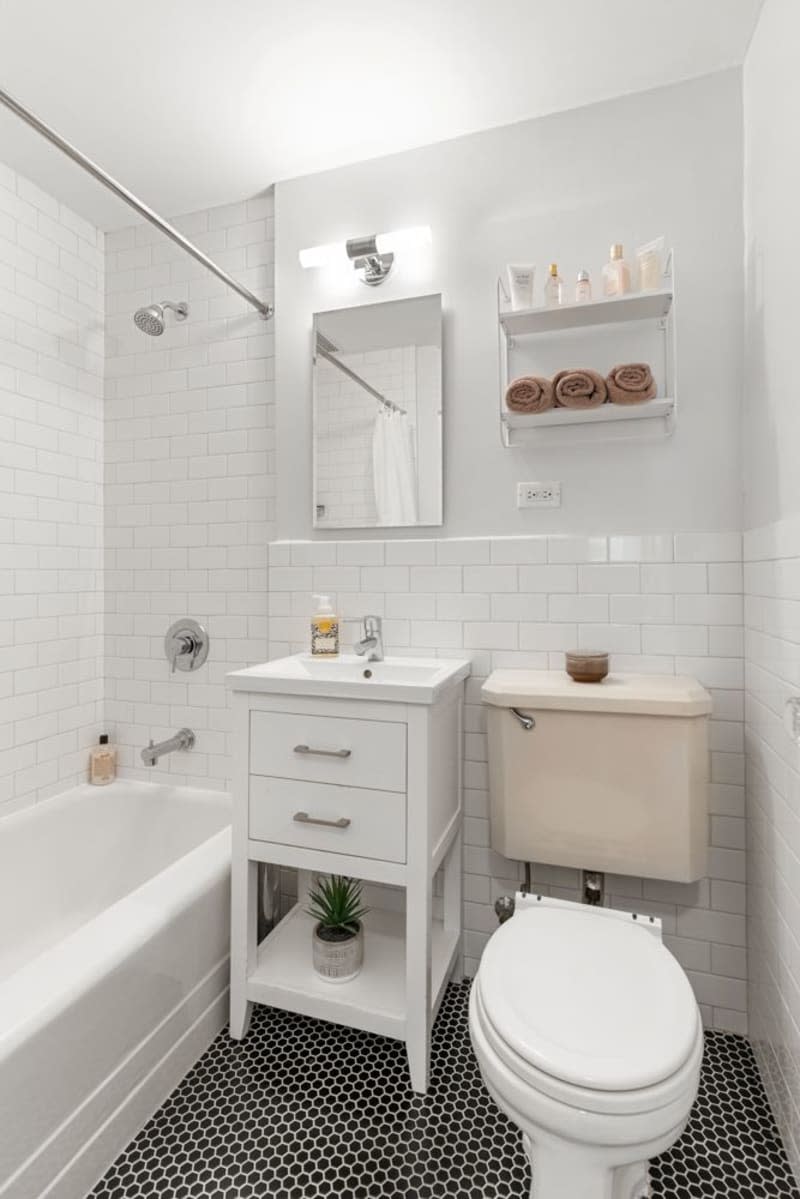 white bathroom with tile half wall and shower and black and white floor