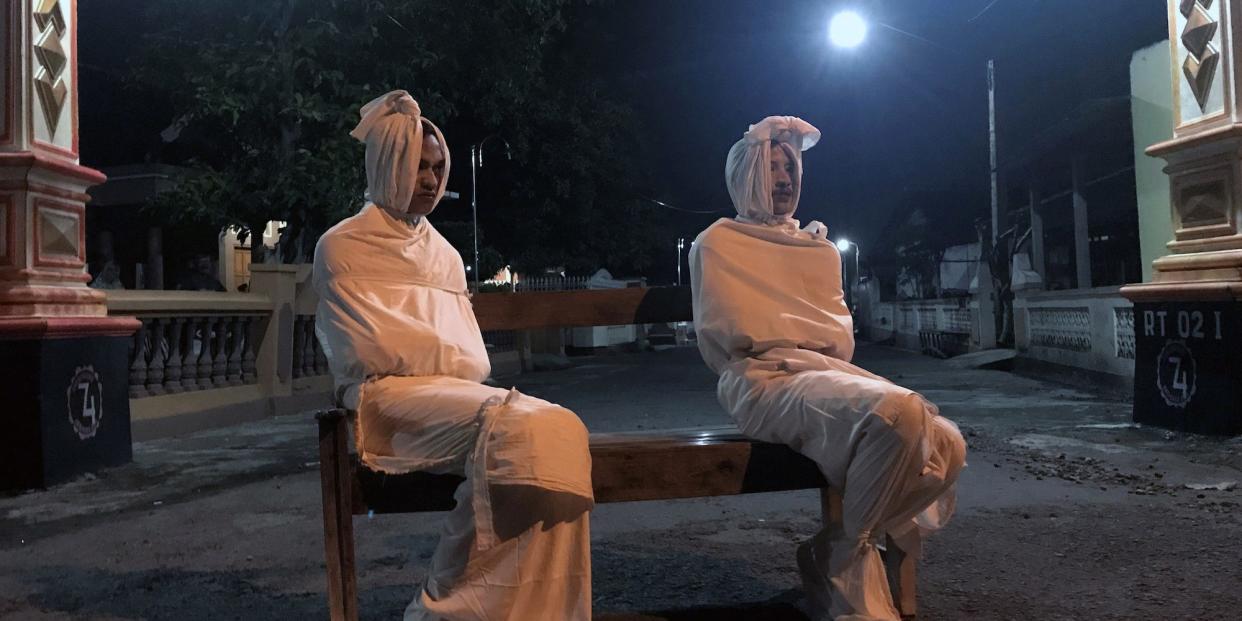 Two volunteers sit on a bench as they play the role of 'pocong', or known as 'shroud ghost', to make people stay at home amid the spread of coronavirus in Indonesia on April 1.