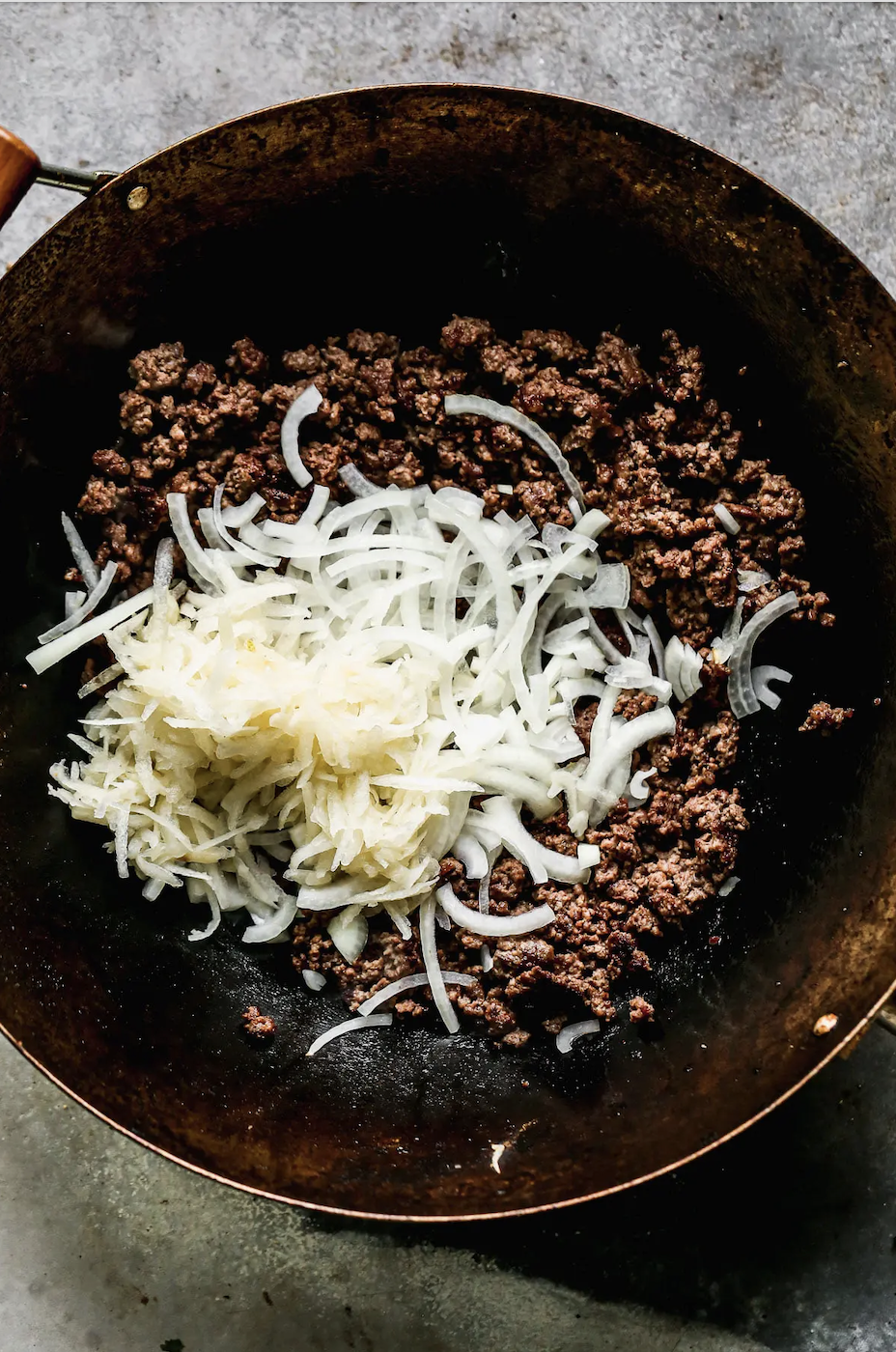 Ground beef and chopped onions in a cooking pan