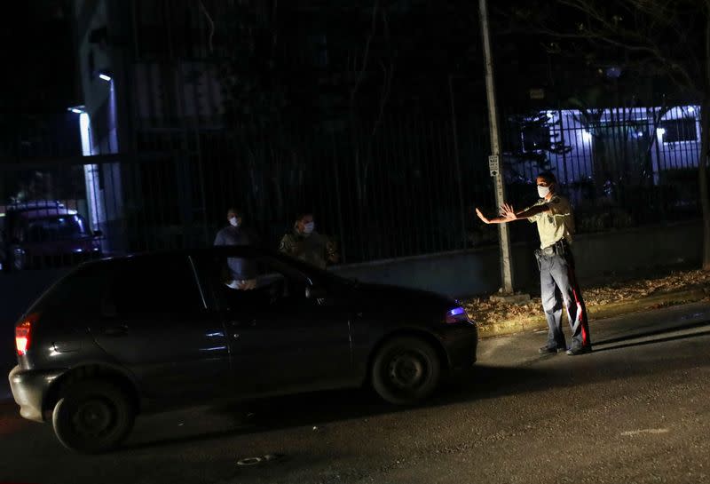 A member of Baruta's municipal police stands in front of a car waiting in line for fuel, during a nationwide quarantine due to the coronavirus disease (COVID-19) outbreak, in Caracas