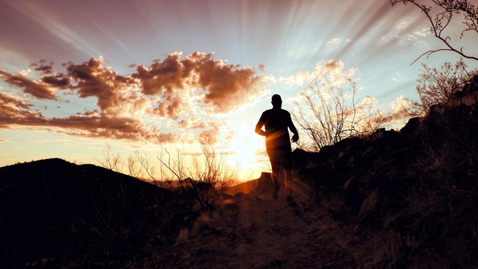 sunrise with rays of light spreading through the clouds while a man runs towards the edge of the hill