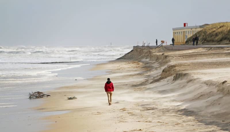 A man walks along the beach below the break-off edge of the last storm surge. Winter storms leave the beaches of Germany's North Sea island without sand. Peter Kuchenbuch-Hanken/dpa