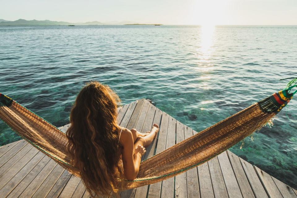 view from behind of woman awakening with ocean view wooden hotel terrace with hammock beautiful morning light