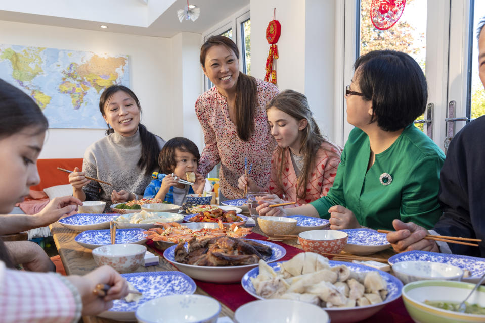 An extended diverse family sitting at a dining table and eating a meal during Chinese New Year at home in Newcastle Upon Tyne, England. The table has a variety of Chinese dishes in different bowls.  Each traditional dish has its own symbolic meaning.  Steamed fish is one of the most famous Chinese New Year dishes.
