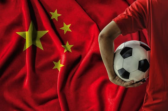 A man holds a soccer ball in front of a Chinese flag.