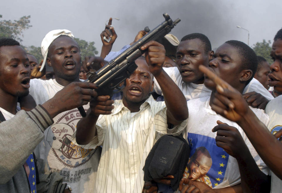 FILE - In this July 27, 2006 file photo shot by AP contributing photographer John Bompengo, looters hold up a gun that was taken from a nearby Church before it was set on fire by supporters of presidential candidate Jean-Pierre Bemba during a rally in Kinshasa, Democratic Republic of Congo. Relatives say longtime Associated Press contributor John Bompengo has died of COVID-19 in Congo's capital. Bompengo, who had covered his country's political turmoil over the course of 16 years, died Saturday, June 20, 2020 at a Kinshasa hospital. (AP Photo/John Bompengo, file)