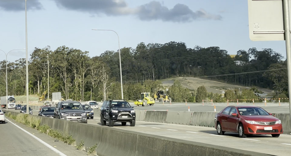 A still of cars on a Gold Coast road. There is clearing in the background.