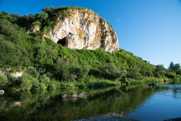 The face of Chagyrskaya Cave in Siberia, abutting a river.