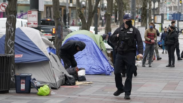 A Seattle police officer walks past tents used by people experiencing homelessness