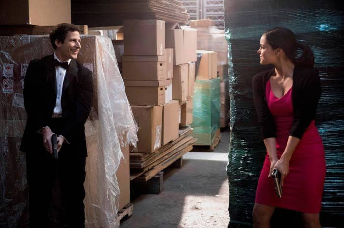 Jake and Amy dressed up with guns drawn in a warehouse