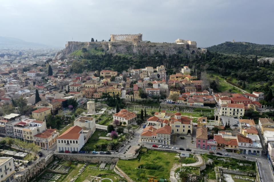 In this Wednesday, April 1, 2020 photo, a view of the Parthenon Temple on top of the Acropolis hills with the deserted Plaka tourist district, in Athens. Deserted squares, padlocked parks, empty avenues where cars were once jammed bumper-to-bumper in heavy traffic. The Greek capital, like so many cities across the world, has seen its streets empty as part of a lockdown designed to stem the spread of the new coronavirus. (AP Photo/Thanassis Stavrakis)