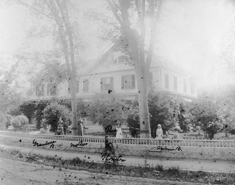 Thornton W. Burgess can just be seen riding a bicycle in front of one of the Sandwich houses where he lived as a child. Other family members, including his mother, can be seen in the yard.