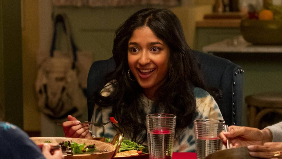 A smiling Devi eats dinner at the table in Never Have I Ever.