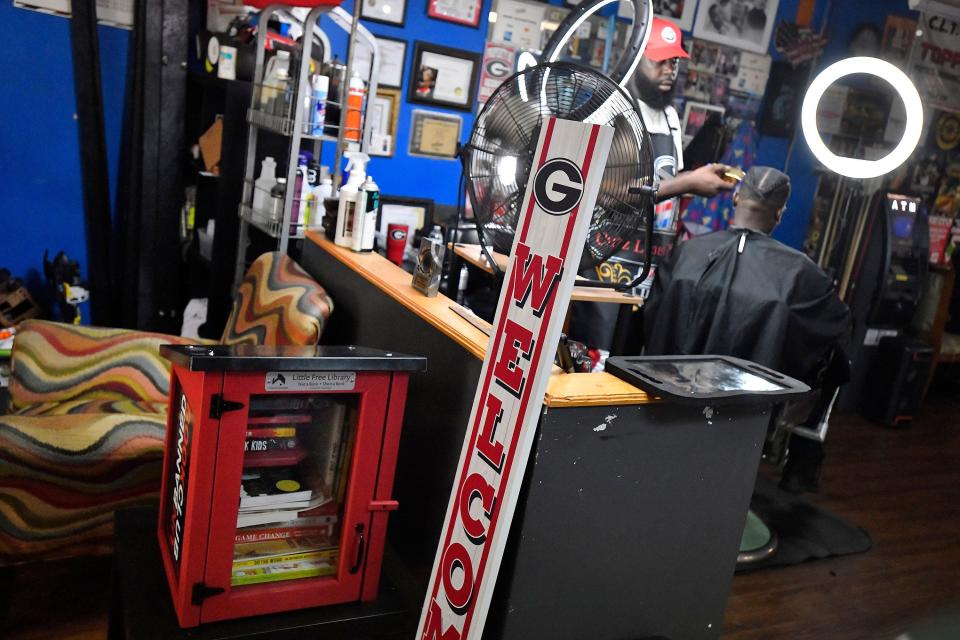 Cedrick Turner works on a client in his barber shop, Cutz-Linez & Trimz at 6050 Moncrief Road on Jacksonville's Northside. The shop is the firt site ifor the Unbanned Bookn Club, a project to distribute books challnged in schools through Little Free Library boxes like the one in the barbershop.