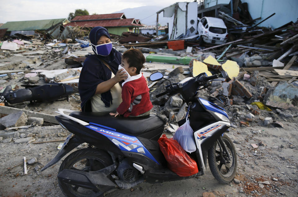 In this Oct. 6, 2018, photo, a woman covers the face of her son as they visit the area where they used to live before a massive earthquake and tsunami hit their seaside village in Palu, Central Sulawesi, Indonesia. The family lost their son. The 7.5 magnitude quake triggered not just a tsunami that leveled huge swathes of the region's coast, but a geological phenomenon known as liquefaction, making the soil move like liquid and swallowing entire neighborhoods. (AP Photo/Aaron Favila)