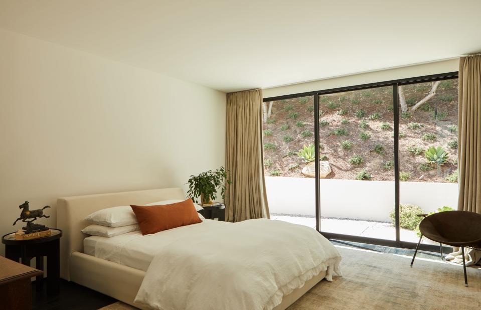 The tones of the custom bed upholstered in cream linen by OSKLO and the antique hand knotted Persian Malayer wool rug from Woven Accents perfectly match, while the colors of the Espresso wood side tables from Holly Hunt and the Hans Olsen midcentury Danish leather Balloon Chair from Orange create contrasts.