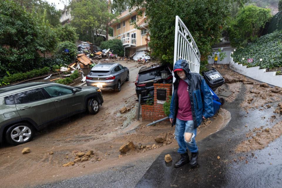 A man and several cars sit outside a home damaged by mudslides in Los Angeles, California on Monday (AFP via Getty Images)