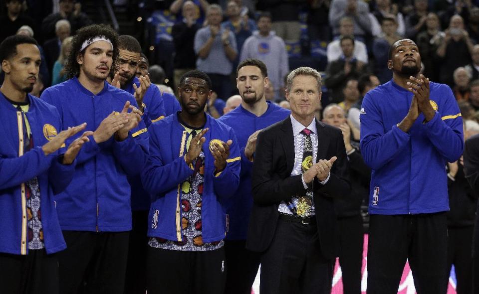 Golden State Warriors coach Steve Kerr, second from right, leads Kevin Durant, right, and other members of the team in applauding the life of Turner Sports NBA sideline reporter Craig Sager, prior to an NBA basketball game against the New York Knicks Thursday, Dec. 15, 2016, in Oakland, Calif. Sager died Thursday after battling cancer. (AP Photo/Ben Margot)