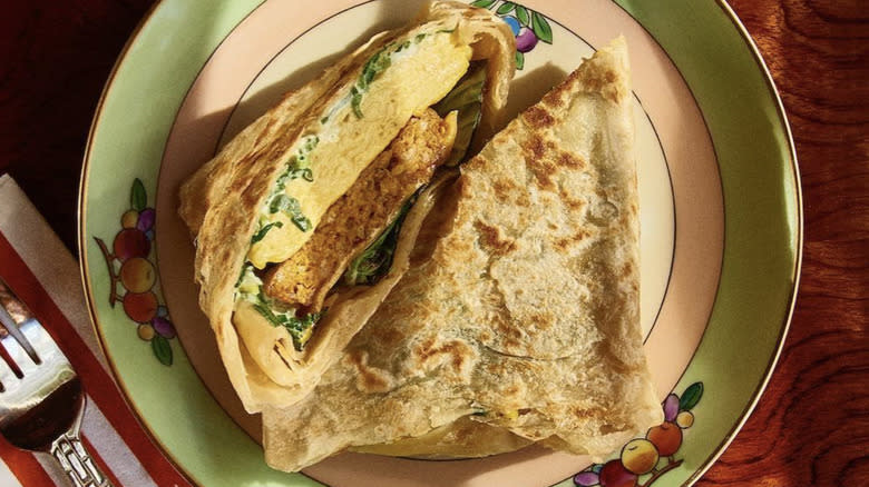 Roti, egg, and sausage sandwich on decorative plate