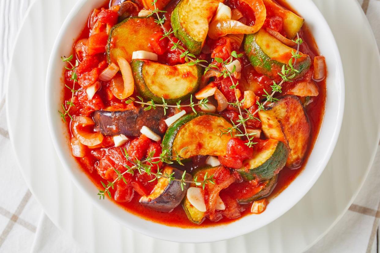 vegetable stew, eggplant, onion, zucchini with tomato sauce, garlic and herbs in a white bowl on a wooden table, landscape view from above, flat lay, macro