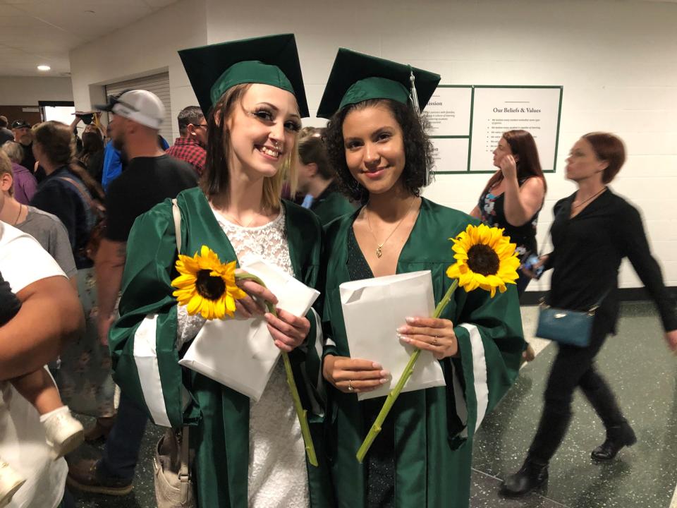 Aliena Carte, left, and Trinity Hatfield, right, hold diplomas and sunflowers after graduating Friday night.